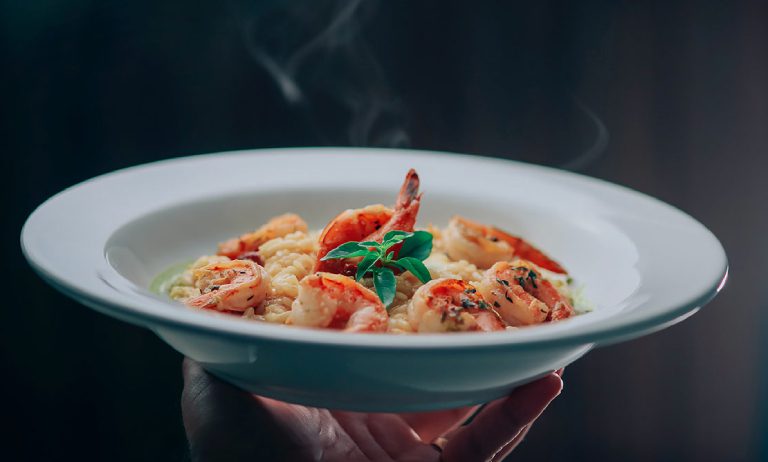 Hand holding a plate of shrimp pasta